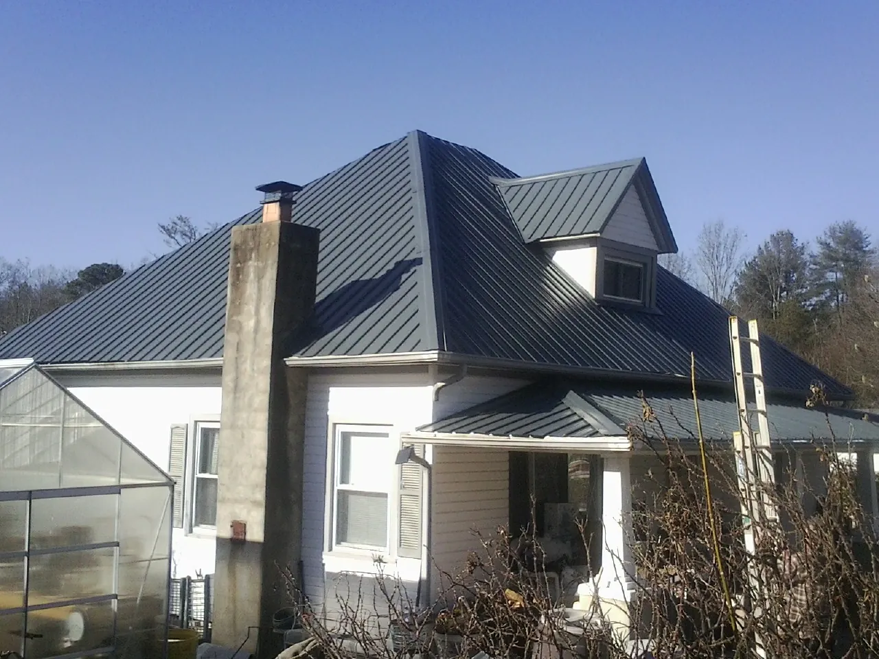 Dark blue standing seam metal roof on a white farmhouse with dormer — Slate & Tile Roof Repair by Roofing Brothers in Cortland