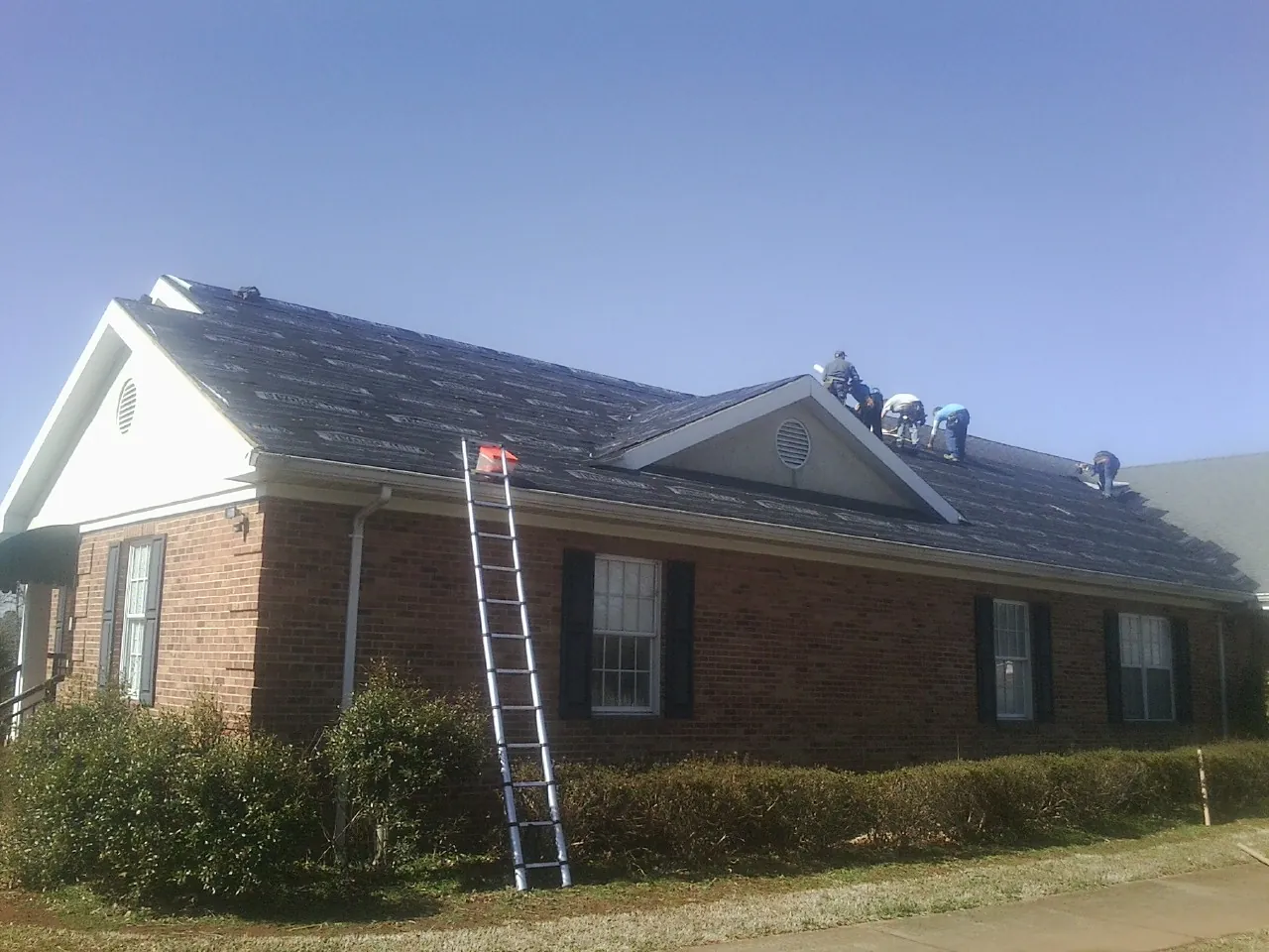 Crew tearing shingles off a brick ranch roof with a ladder set — Metal Roof Repair work by our crew in Cortland