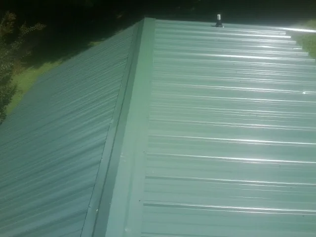 New green metal panels meeting at the ridge of a roof — Flat Roof Repair work by our crew in Cortland