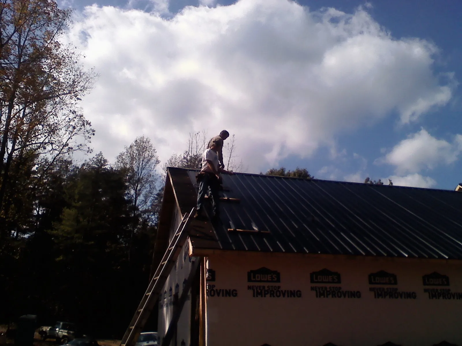 Roofer fastening dark metal panels high against a cloudy sky, from a Roof Inspection job in Cortland