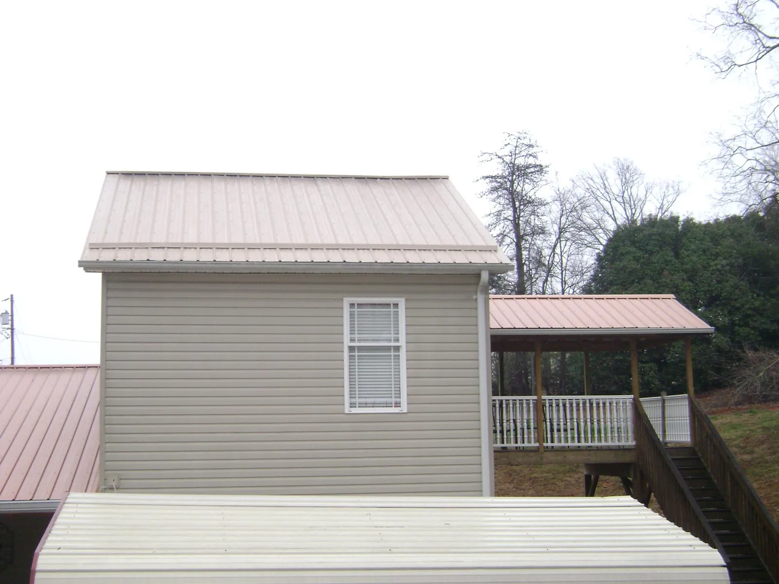 Tan metal roofs on a two story addition and attached porch, from a Roof Replacement job in Cortland